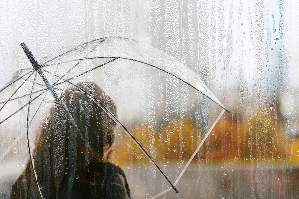 A woman silhouette with transparent umbrella through wet window with drops of rain. Autumn