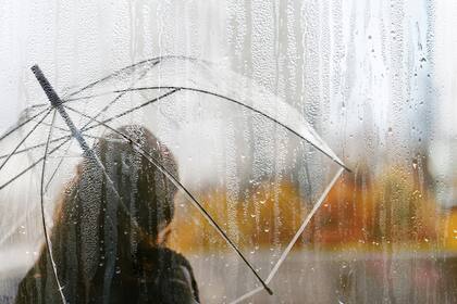 A woman silhouette with transparent umbrella through wet window with drops of rain. Autumn
