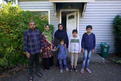 Abdul (izquierda), quien trabajaba como mecánico antes de salir de Kabul, Afganistán, junto con su familia hace un mes, posa para una foto el jueves 16 de septiembre de 2021 con su familia frente a la casa que se les ha facilitado para quedarse en Seattle. (AP Foto/Ted S. Warren)