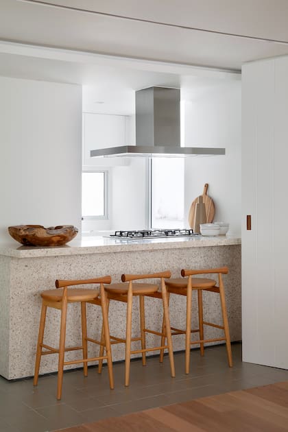 Acá el estudio propuso un juego de materialidades con pisos de cerámico, una isla de terrazo y banquetas de madera. El extractor metálico suma un contrapunto.