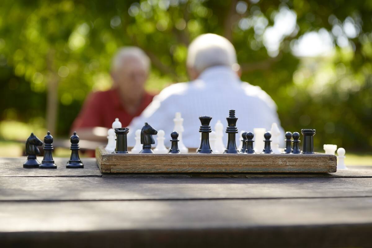 Active retirement, old friends and leisure, two senior men having fun and playing chess game at park. Focus on chessboard in foreground