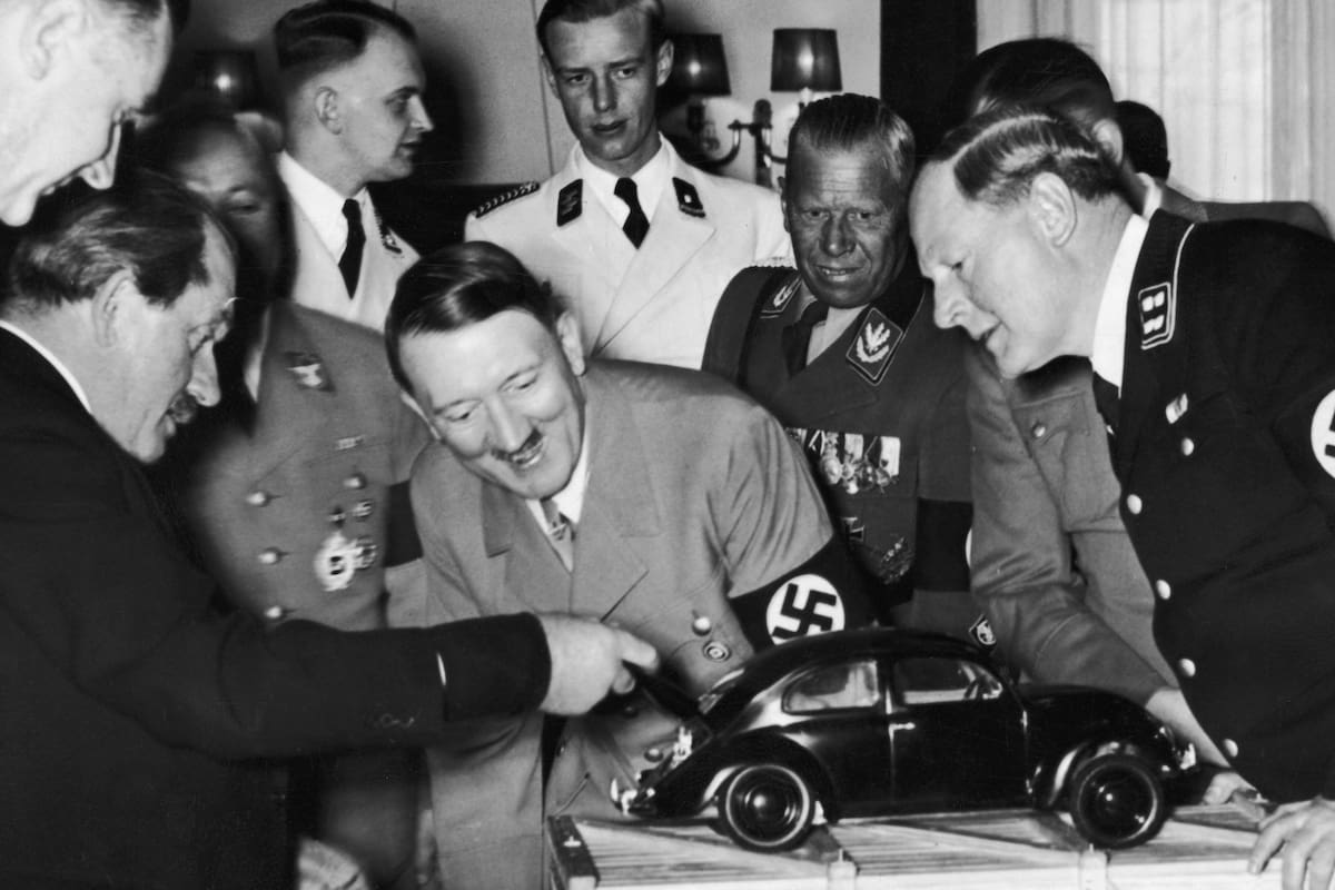 Adolf Hitler observa una maqueta del "auto del pueblo" y se ríe al descubrir al motor en la parte trasera. Quien levanta la tapa del baúl es el diseñador Ferdinand Porsche