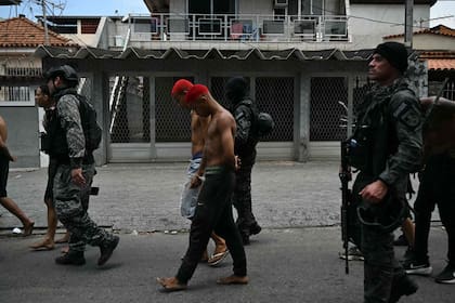 Agentes de policía escoltan a sospechosos arrestados durante la Operación Contención fuera de la favela Vila Cruzeiro, en el complejo Penha