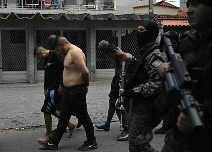 Agentes de policía escoltan a sospechosos arrestados durante la Operación Contención fuera de la favela Vila Cruzeiro