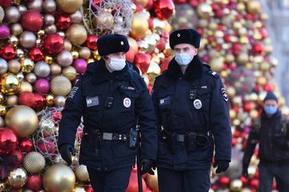 Agentes de policía rusos con mascarillas patrullan junto a las decoraciones festivas para las próximas vacaciones de Año Nuevo y Navidad en Moscú el 9 de diciembre de 2020, en medio de la pandemia de coronavirus