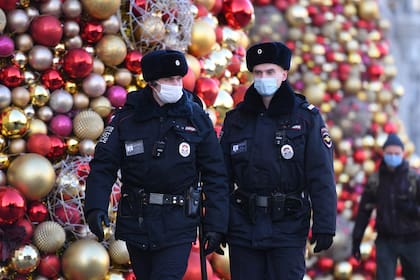 Agentes de policía rusos con mascarillas patrullan junto a las decoraciones festivas para las próximas vacaciones de Año Nuevo y Navidad en Moscú el 9 de diciembre de 2020, en medio de la pandemia de coronavirus