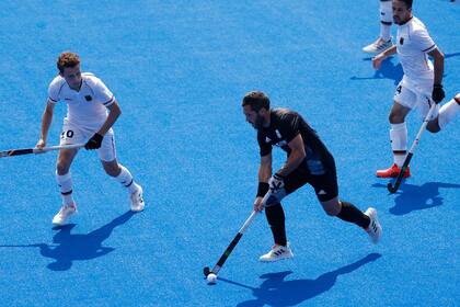 Agustín Mazzilli maniobra con la bocha ante la marca de los defensores alemanes durante el partido entre los Leones y los teutones, por cuartos de final del hockey sobre césped de Tokio 2020.