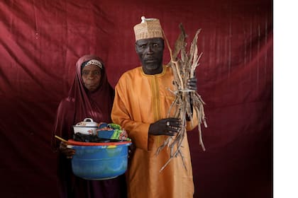 Aisha Umaru sostiene un recipiente de leche mientras Umari Usman Kaski sostiene leña en el campo de desplazados internos de Bakasi, Maiduguri, Nigeria