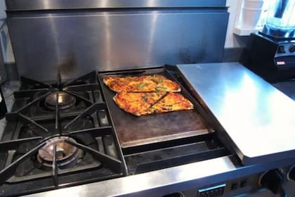 Al no tener un horno tostador, que suele ser la opción preferida para recalentar pizza, optó por usar una plancha, cubriéndola con la tapa de acero inoxidable que sirve para ocultarla cuando no está en uso (Serious Eats)