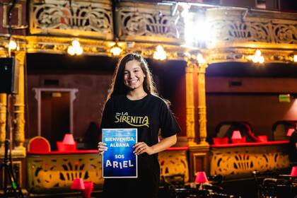 Albana Fuentes sonríe frente a cámara con una remera de La sirenita y un cartel que le da la bienvenida al papel que interpretará en el musical: la princesa Ariel