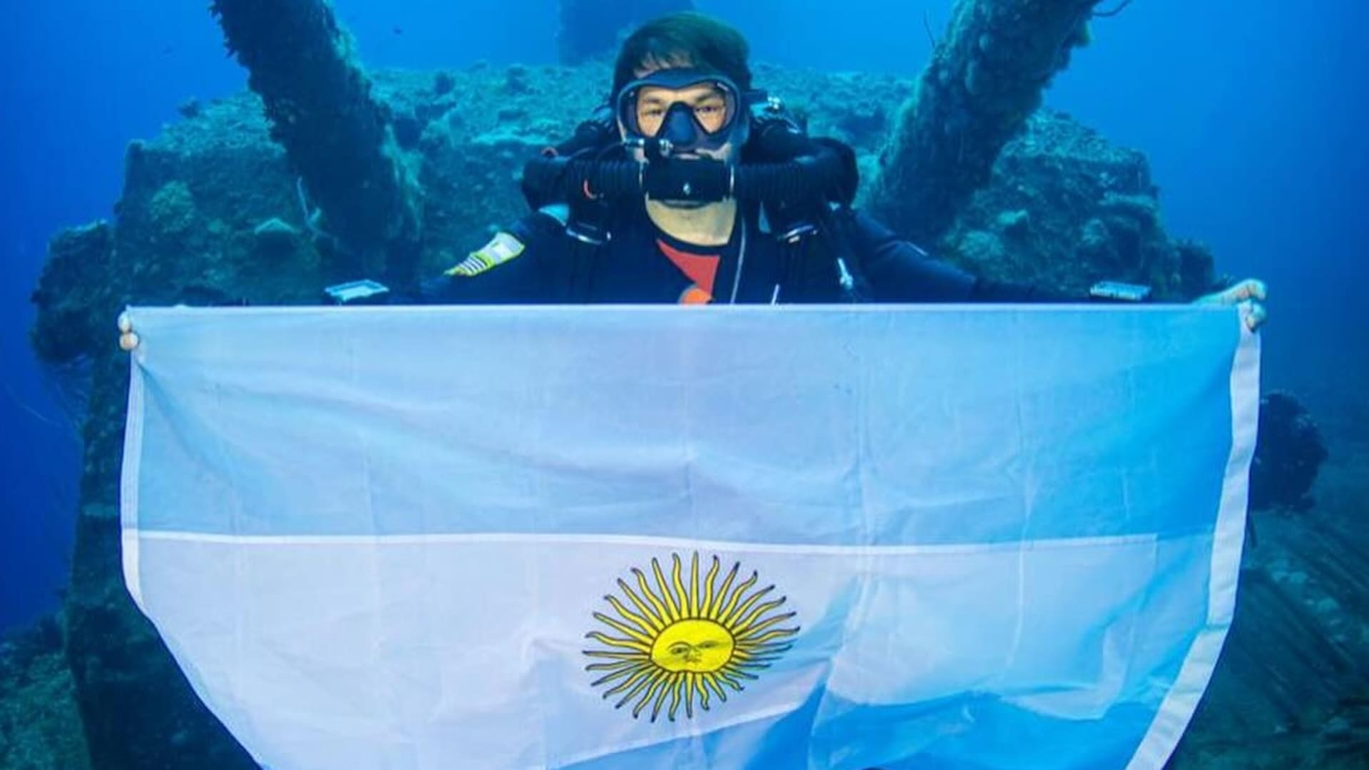 Alejandro Dutto con la bandera argentina en la cubierta del portaaviones de los Estados Unidos, USS Saratoga, en lo profundo de la laguna del atolón Bikini, en el Oceáno Pacífico