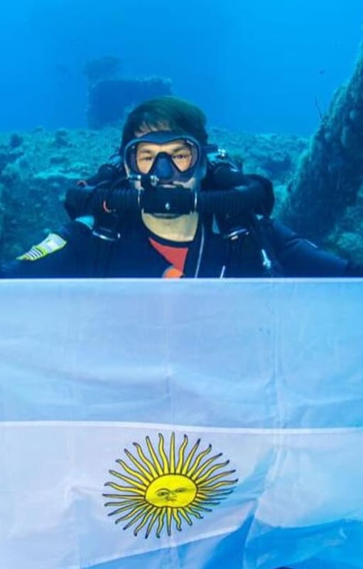 Alejandro Dutto con la bandera argentina en la cubierta del portaaviones de los Estados Unidos, USS Saratoga, en lo profundo de la laguna del atolón Bikini, en el Oceáno Pacífico