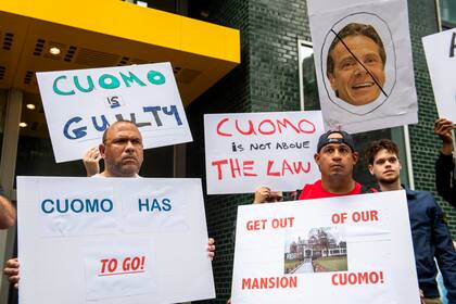 Algunos manifestantes sostienen unos letreros afuera de la oficina del gobernador de Nueva York, Andrew Cuomo, exigiendo su renuncia, el miércoles 4 de agosto de 2021, en Nueva York. (AP Foto/Brittainy Newman)