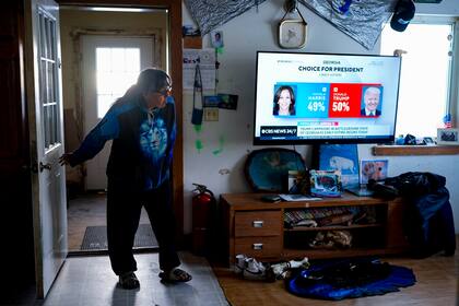 Alice Aishanna entra en su salón mientras una emisión de CBS News muestra a la candidata presidencial demócrata Kamala Harris y al candidato presidencial republicano, el expresidente Donald Trump, el martes 15 de octubre de 2024, en su casa de Kaktovik, Alaska. (AP Foto/Lindsey Wasson)