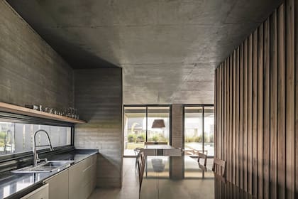 La ventana sobre la mesada y el comedor contiguo definen con su luz el clima de un espacio neutro que encuentra su expresión en el reflejo de esa leve claridad sobre los planos de color negro.