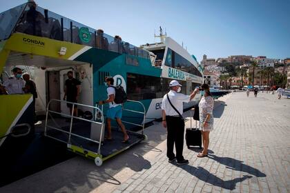 An employee takes the temperature of a passenger before boarding a ferry at Ibiza´s harbour, on July 31, 2020. - Spain plunged into recession in the second quarter after its gross domestic product tumbled by 18.5 percent due to the coronavirus pandemic, official figures showed.