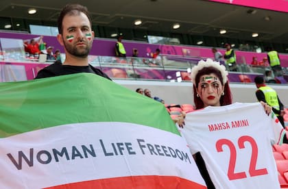Una partidaria de Irán con lágrimas de sangre maquilladas en la cara sostiene una camiseta de fútbol en la que se lee el nombre de Mahsa Amini, la mujer kurda iraní de 22 años que murió en el hospital después de ser arrestada por la policía moral por violar el estricto código de vestimenta de Irán. posa con otro seguidor que sostiene una bandera que dice "Libertad de vida de la mujer" mientras asisten al partido de fútbol del Grupo B de la Copa Mundial de Qatar 2022