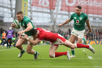 Andrew Conway de Irlanda, cruza la línea para anotar un ensayo cuando es derribado por Josh Adams de Gales.