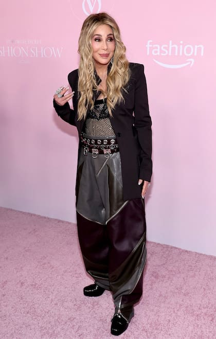 Antes del desfile, Cher desfiló por la alfombra rosa con un cambio de look: cambió su clásico pelo negro por un tono rubio. En cuanto al outfit, optó por un traje que combinó varios géneros en gris y negro, con pantalones tipo bombacha de campo y un cinturón en cuero