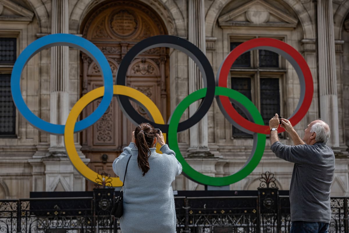 ARCHIVO - Dos personas toman fotos de los anillos olímpicos en el ayuntamiento de París, el 30 de abril de 2023. (AP Foto/Aurelien Morissard)
