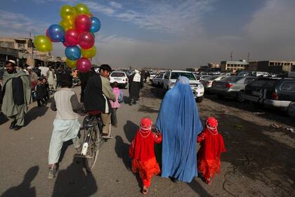 ARCHIVO - En esta foto de archivo del 3 de enero de 2011, un vendedor de globos pasa en su bicicleta junto a una mujer que agarra a dos niñas en un mercado de Kabul, Afganistán. (AP Foto/Altaf Qadri, Archivo)