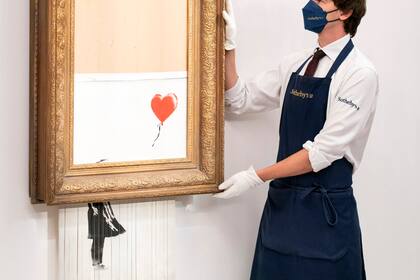 ARCHIVO - En esta foto del 3 de septiembre de 2021, un manipulador de arte sostiene "Love is in the Bin" de Banksy en la casa de subastas Sotheby's en Londres. La obra, que se autodestruyó de manera sensacional justo después de venderse por 1,4 millones de dólares, se ofrece de nuevo en subasta el jueves 14 de octubre con un precio de venta estimado en 4 a 6 millones de libras esterlinas (5,5 a 8,3 millones de dólares). (Dominic Lipinski/PA vía AP)
