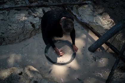 ARCHIVO - En esta fotografía de archivo del 21 de agosto de 2020, un minero utiliza un recipiente para separar fragmentos de oro de la tierra con agua en una mina ilegal en la selva amazónica, en la zona de Itaituba, estado de Pará, en Brasil. (AP Foto/Lucas Dumphreys, Archivo)