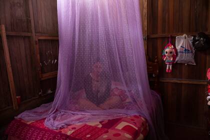 ARCHIVO - En esta fotografía de archivo del martes 29 de septiembre de 2020, Valentina Esperanza, que se recupera de dengue, permanece sentada en su cama protegida con un mosquitero mientras ve un programa de televisión en su casa en la ciudad de Pucallpa, departamento de Ucayali, en Perú. (AP Foto/Rodrigo Abd)