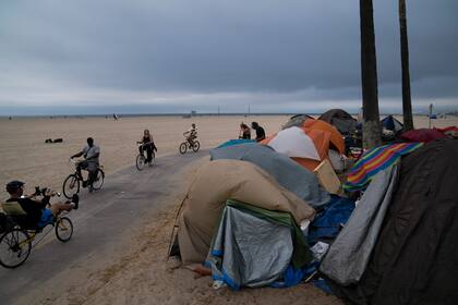 ARCHIVO - En esta fotografía del 29 de junio de 2021 varias personas pasean en bicicleta frente a un campamento de indigentes en Los Ángeles. (AP Foto/Jae C. Hong, Archivo)