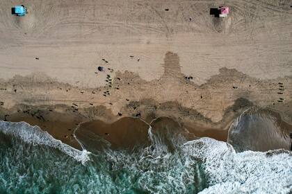 ARCHIVO - Esta fotografía tomada con un dron muestra desde las alturas a bañistas mientras trabajadores con trajes protectores continúan limpiando las partes contaminadas con crudo en la playa de la localidad de Huntington Beach, California, el 11 de octubre de 2021. (AP Foto/Ringo H.W. Chiu, Archivo)