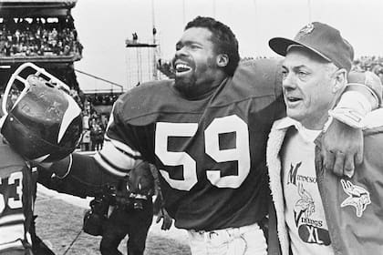 ARCHIVO ' Foto del 14 de diciembre de 1980, el entrenador de los Vikings de Minnesota Bud Grant sonríe mientras se dirige al vestuario abrazado del linebacker Matt Blair tras vencer a los Browns de Cleveland. El sábado 11 de marzo del 2023, Grant fallece a los 95 años. (AP Foto/File)