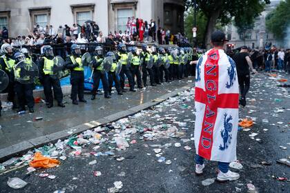 ARCHIVO - Foto del domingo 11 de julio del 2021, seguidor de Inglaterra porta la bandera frente a una línea de policías en Trafalgar Square. El viernes 14 de junio del 2024, la policía francesa considera el duelo de Inglarerra ante Serbia de alto riesgo. (AP Foto/Peter Morrison, Archivo)
