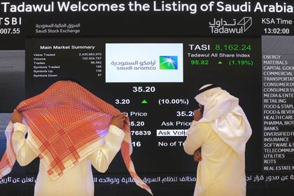 ARCHIVO - Funcionarios de la bolsa saudí miran la pantalla de cotizaciones que muestra a la petrolera estatal saudí Aramco, tras la oferta pública inicial de la compañía en la bolsa, en Riad, Arabia Saudí, el 11 de diciembre de 2019. (AP Foto/Amr Nabil, Archivo)