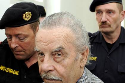 ARCHIVO - Josef Fritzl, en el centro, es escoltado en el cuarto día de su juicio en la corte provincial del St. Poelten, Austria, el jueves 19 de marzo de 2009. Jueces austriacos concluyeron que un hombre que mantuvo cautiva a su hija durante 24 años, la violó miles de veces y tuvo siete hijos con ella puede ser trasladado de un centro de detención psiquiátrica a una prisión convencional, según indicó una corte el martes. (AP Foto/Robert Jaeger, Pool, Archivo)