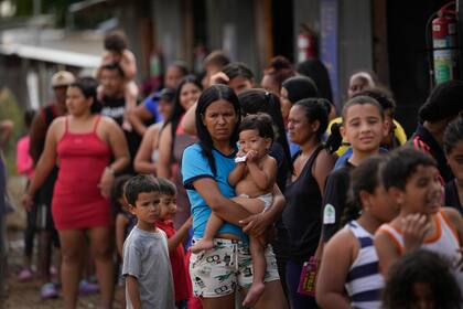 ARCHIVO - La migrante venezolana Minorca Parra sostiene a su hija Karin Alvear mientras hace fila para recibir alimentos en un campamento temporal después de cruzar el Tapón del Darién desde Colombia en Lajas Blancas, Panamá, el 27 de junio de 2024. La migración a través del Tapón del Darién que divide a Colombia y Panamá ha disminuido significativamente este mes desde que el presidente panameño José Raúl Mulino asumió el cargo y ordenó a las autoridades tomar el control de la densa selva fronteriza, dijo la policía fronteriza del país el miércoles 17 de julio de 2024. (AP Foto/Matías Delacroix, Archivo)
