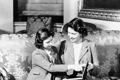 ARCHIVO - La princesa Margarita (izquierda) señala una parte de un libro sostenido por su hermana, la princesa Isabel, en el Palacio de Buckingham, el 14 de agosto de 1942. (AP Foto, Archivo)