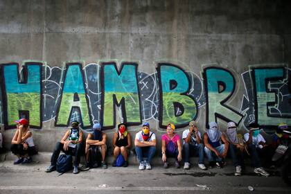 ARCHIVO - Manifestantes antigubernamentales se sientan debajo de un puente que tiene un grafiti durante una protesta en Caracas, Venezuela, el 1 de julio de 2017. Un informe de las Naciones Unidas publicado el martes 30 de noviembre de 2021, dice que América Latina se ha convertido en la región con el crecimiento más rápido en los niveles de hambre, el peor en dos décadas. (AP Foto/Ariana Cubillos, Archivo)
