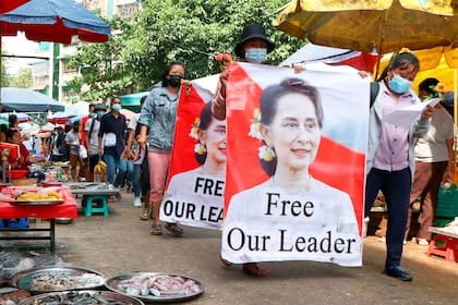 ARCHIVO - Manifestantes caminan por un mercado con carteles de la depuesta líder de Myanmar Aung San Suu Kyi, en el muncipio de Kamayut, en Yangón, Myanmar, el 8 de abril de 2021. (AP Foto, Archivo)