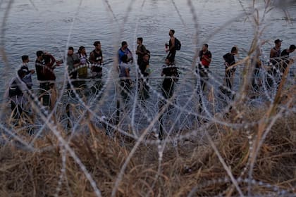 ARCHIVO - Migrantes esperan junto a una barrera de alambre de púas tras haber cruzado el rio Bravo (o Grande) desde el lado mexicano hacia Estados Unidos en Eagle Pass, Texas, el 23 de septiembre de 2023. (AP Foto/Eric Gay, Archivo)