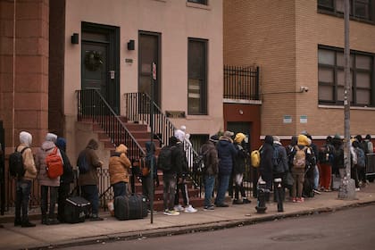 ARCHIVO - Migrantes hacen cola en el frío mientras buscan un refugio fuera de un centro de asistencia a migrantes en la escuela primaria St. Brigid, el 5 de diciembre de 2023, en Nueva York. (AP Foto/Andres Kudacki, Archivo)