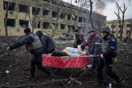 ARCHIVO - Rescatistas y voluntarios llevan a una mujer herida desde un hospital de maternidad que resultó dañado por proyectiles en Mariúpol, Ucrania, el 9 de marzo de 2022.  (AP Foto/Evgeniy Maloletka, Archivo)