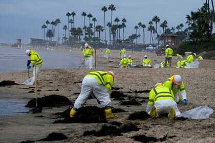 ARCHIVO - Trabajadores en trajes de protección limpian una playa contaminada de Corona del Mar, en el sur de California, el 7 de octubre de 2021. (AP Foto/Ringo H.W. Chiu, Archivo)