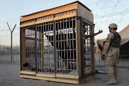 ARCHIVO - Un detenido en una celda de confinamiento solitario al aire libre habla con un soldado en la prisión de Abu Ghraib en las afueras de Bagdad, Irak, el 22 de junio de 2004. (AP Foto/John Moore, Archivo)