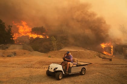 ARCHIVO - Un vecino monta en un vehículo de golf a su salida de su propiedad mientras el incendio Canyon arde el 7 de agosto de 2025, en Hasley Canyon, California