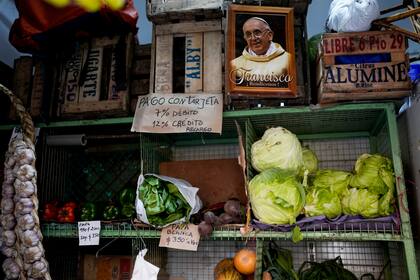 ARCHIVO - Una foto del papa Francisco colocada junto a un cartel que avisa del costo de pagar con tarjeta de débito o crédito en un mercado de frutas y verduras de Buenos Aires, Argentina, el jueves 11 de mayo de 2023. Según un reporte del Instituto Nacional de Estadísticas y Censos publicado el jueves 13 de julio de 2023, en junio, Argentina reportó una inflación del 6%, la más baja desde que empezó el año, a partir de una estabilización en los precios de los alimentos. (Foto AP/Natacha Pisarenko, Archivo)