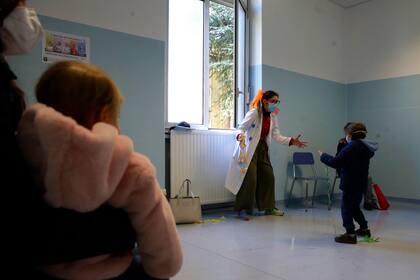 Archivo - Una mujer con disfraz de payaso entretiene a niños antes de que reciban la vacuna contra la influenza en un hospital militar en Milán, Italia, el viernes 20 de noviembre de 2020. (AP Foto/Luca Bruno, Archivo)
