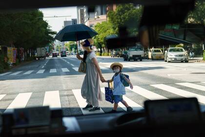 ARCHIVO - Una peatona que cruza una calle con una niña es retratada a través de la ventanilla de un taxi en Tokio, el lunes 19 de julio de 2021. (AP Foto/David Goldman, Archivo)