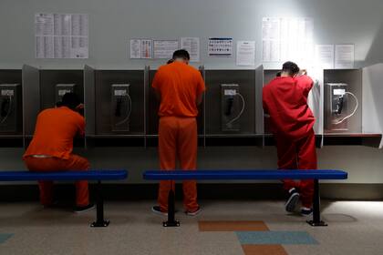 ARCHIVO - Unos detenidos hablan por teléfono en el centro de detención del Servicio de Control de Inmigración y Aduanas de Estados Unidos en Adelanto, California, el 28 de agosto de 2019. (AP Foto/Chris Carlson, Archivo)