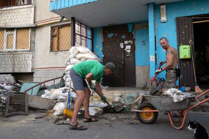 ARCHIVO - Viktor Lazar, a la derecha, limpia la calle ante su apartamento en el distrito de Saltivka tras ataques rusos en Járkiv, Ucrania, el 5 de julio de 2022. (AP Foto/Evgeniy Maloletka, Archivo)