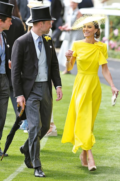 Kate apostó a un clásico de su guardarropa: el vestido Brigitte de Roksanda, en crêpe y seda, con drapeado y lazo en el escote. Lo completó con un tocado estilo plato, pulsera de tres hileras de perlas –heredada de su suegra, Lady Diana–, pendientes de perlas y diamantes y stilettos de Gianvito Rossi. A su lado, el príncipe William, elegantísimo con un toque amarillo en la solapa